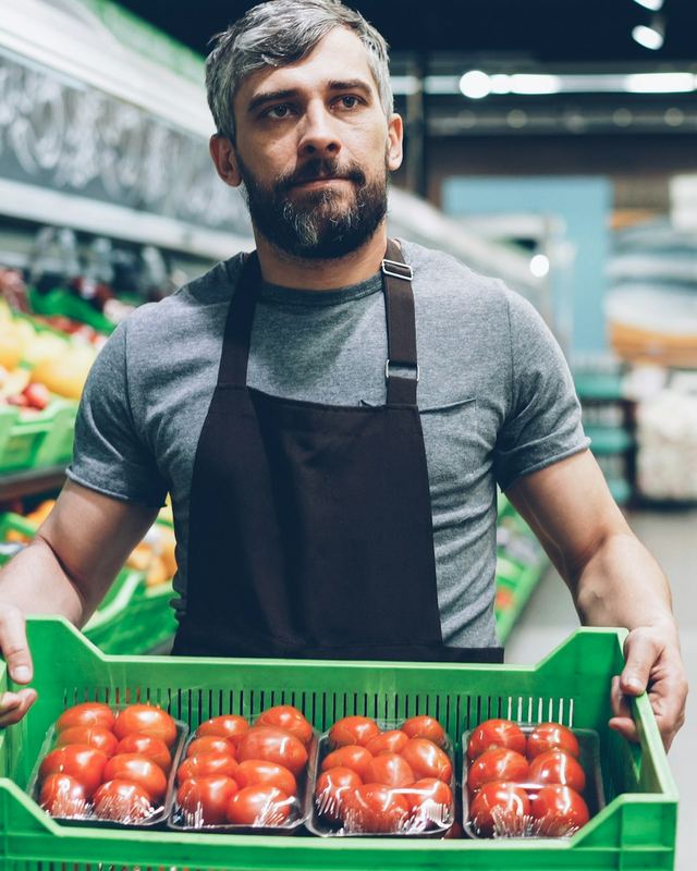 Verkäufer trägt eine Kiste Tomaten durch den Markt
